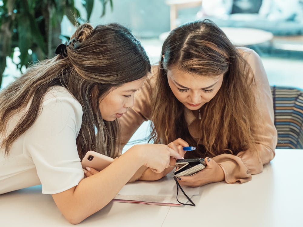 Two women looking at a phone together, sharing a genuine moment of connection — representing real friendship beyond app swipes