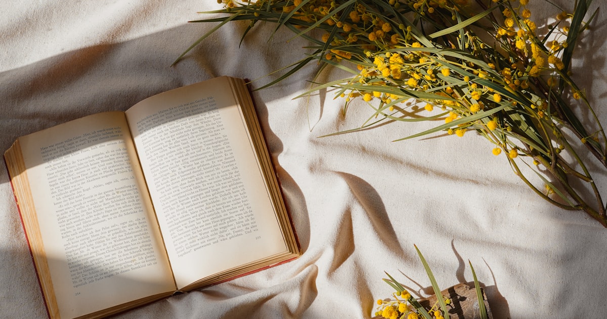 A cozy reading setup with a book, flowers, and tea