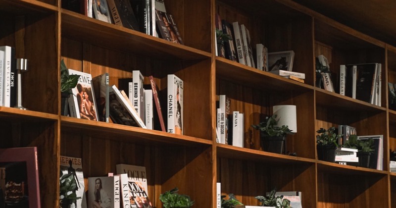 A shelf of books and trailing houseplants in a warm interior