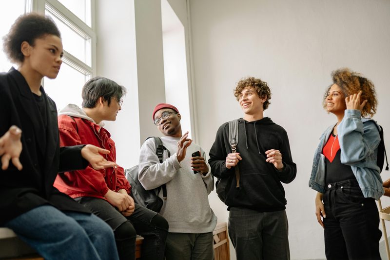 Five diverse friends talking and laughing together indoors by a large window