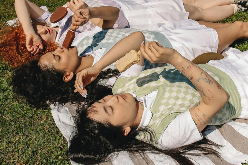 Two women lying on grass in the sunshine, relaxed and laughing together