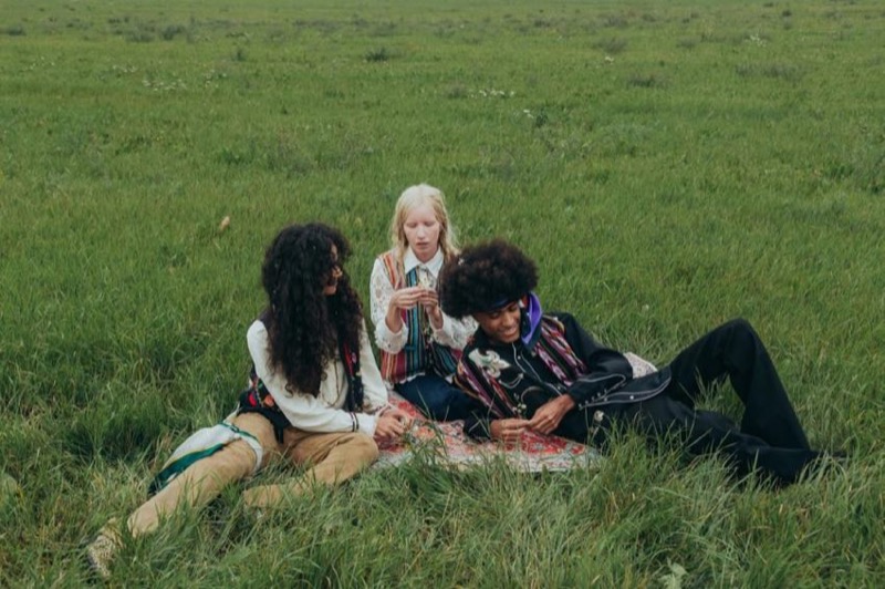 Three friends sitting together on a blanket in a wide grassy meadow
