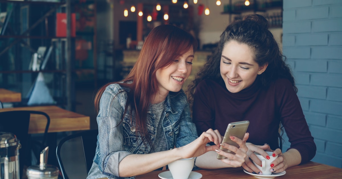 Two friends smiling while looking at a phone screen together