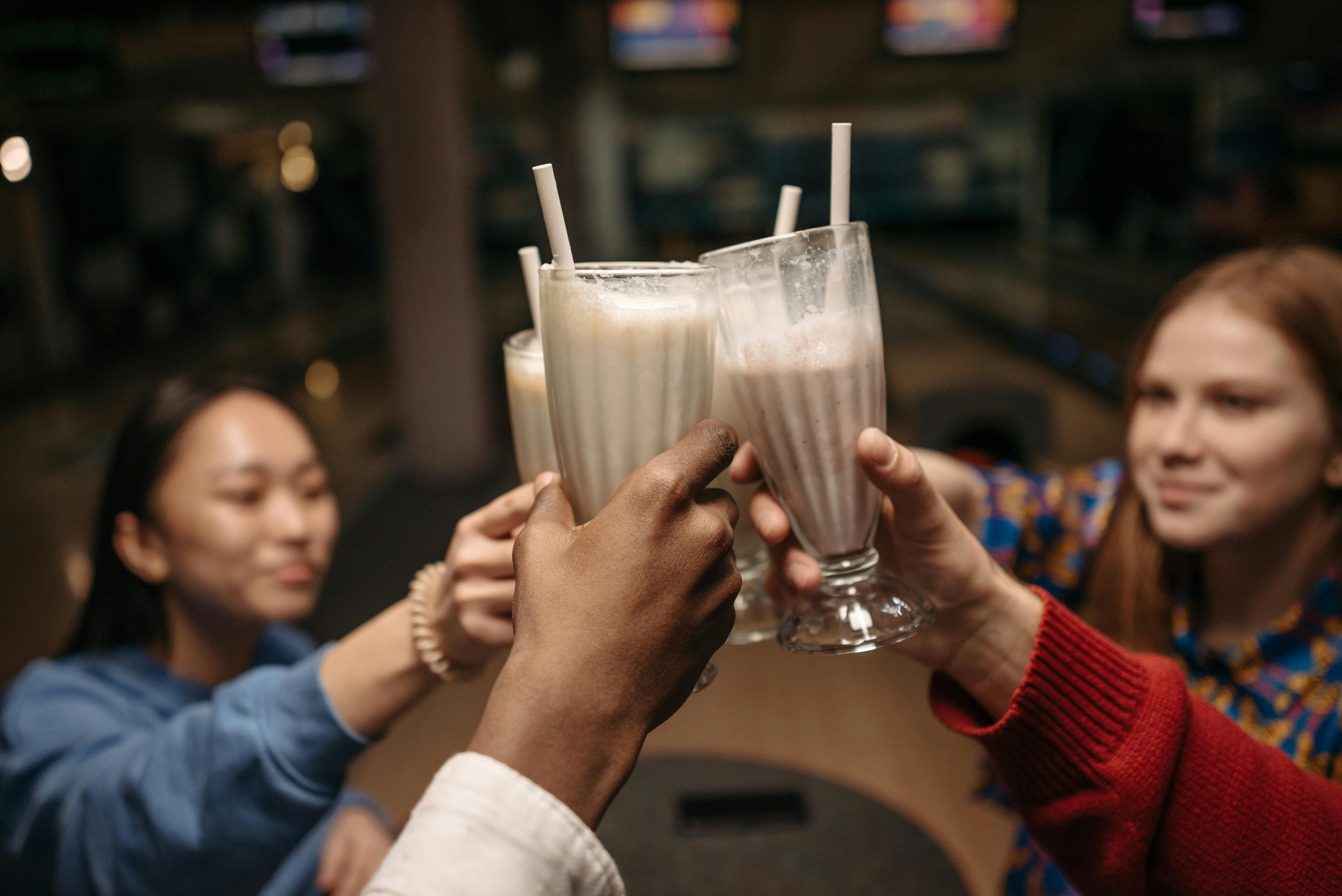 Friends clinking milkshakes together at a bowling alley, laughing