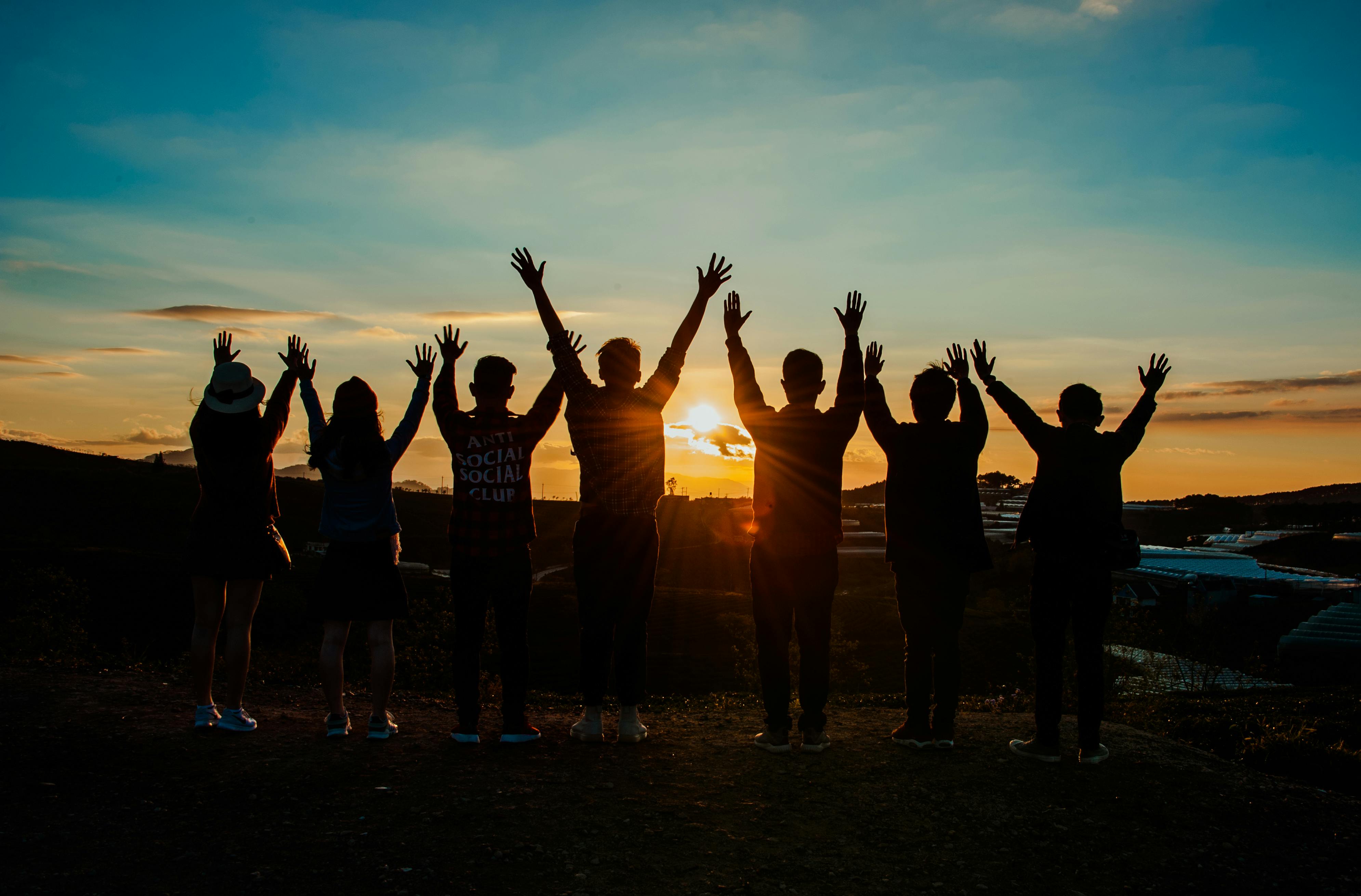 Silhouettes of a group of friends at sunset with hands raised, bittersweet
