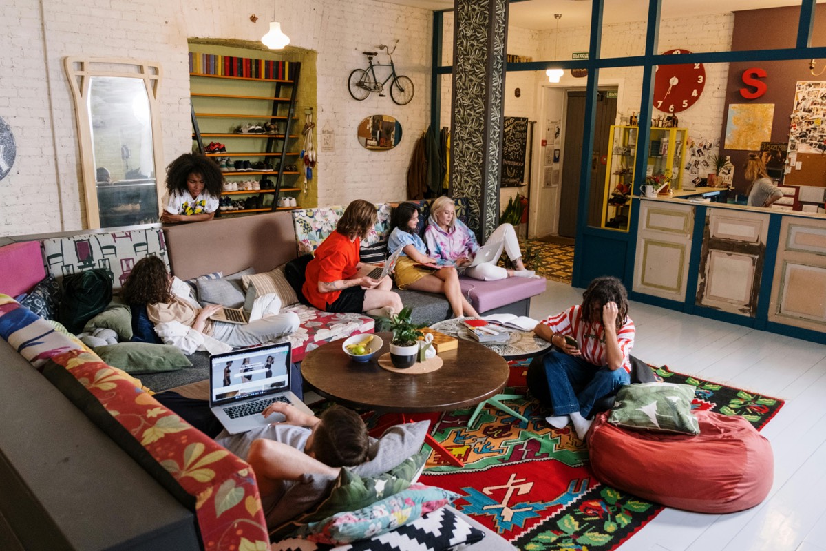 Diverse group of adults working and socializing in a cozy community space with laptops, books, and casual seating arrangements