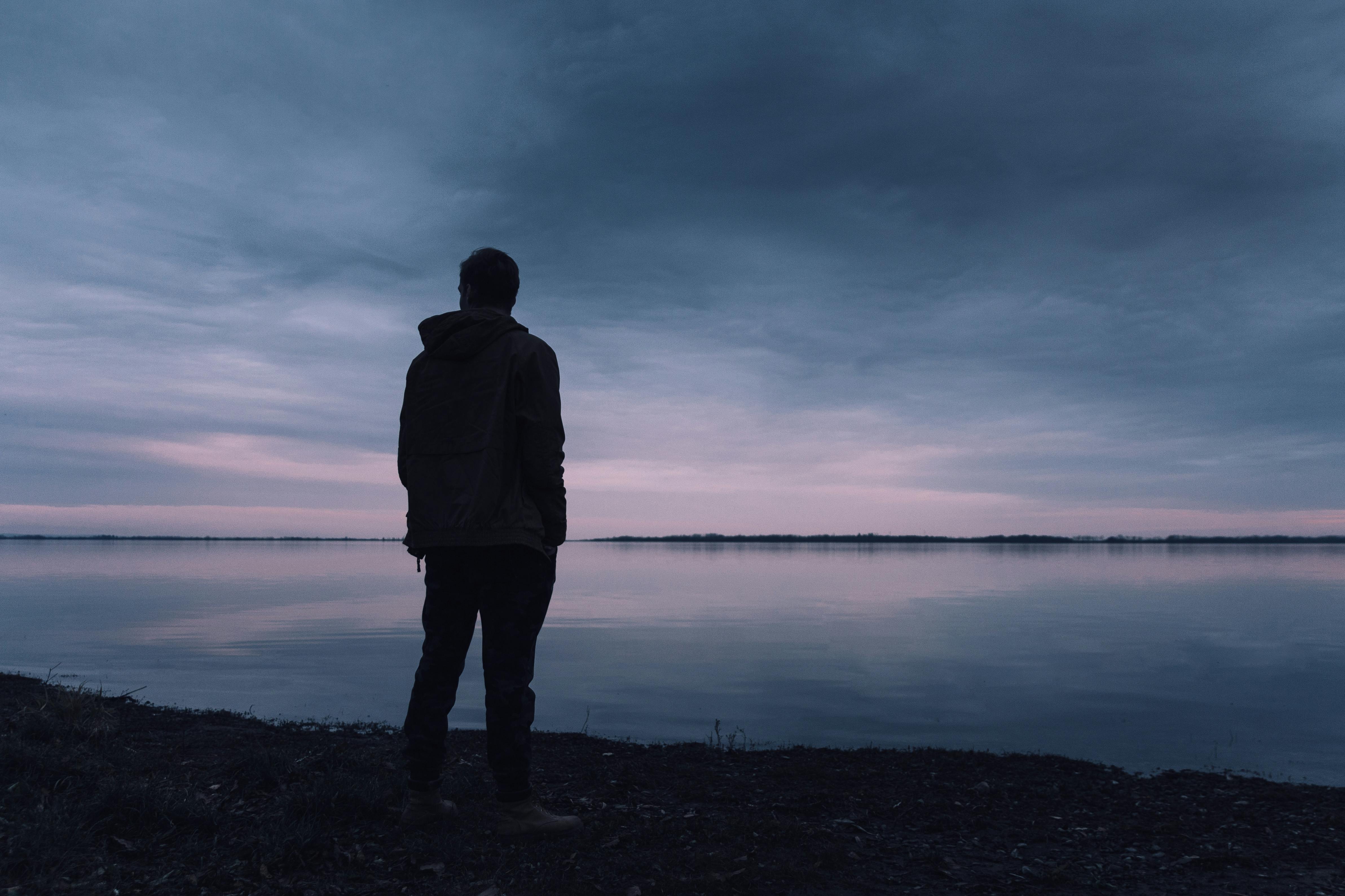 Silhouette of a person standing alone by a lake at dusk, reflecting