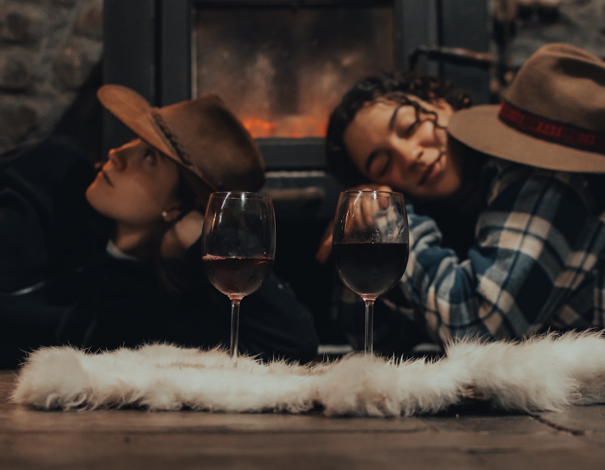Two people sitting by a fireplace with wine glasses, cozy and warm