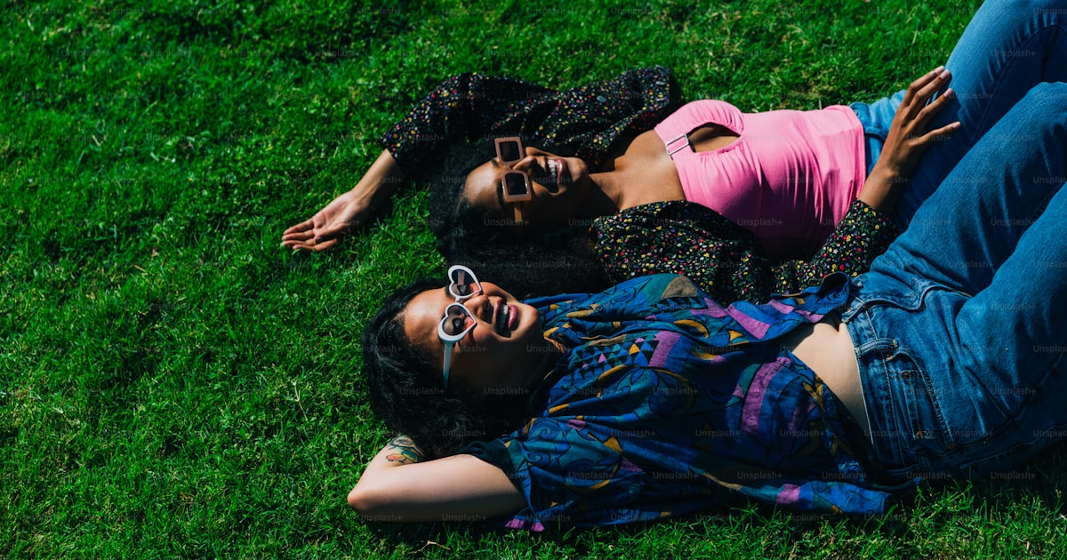 Two women on a bright green grassy field, sunglasses, colorful and sunny