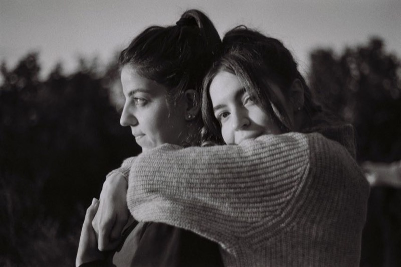 Two women in black and white embracing closely outdoors