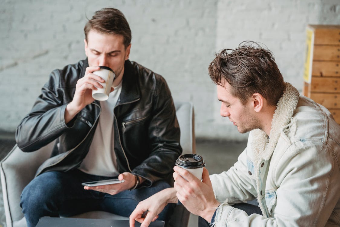 Two friends sitting together with coffee, having a candid and relaxed conversation — the kind of genuine connection that gets harder to find after 25